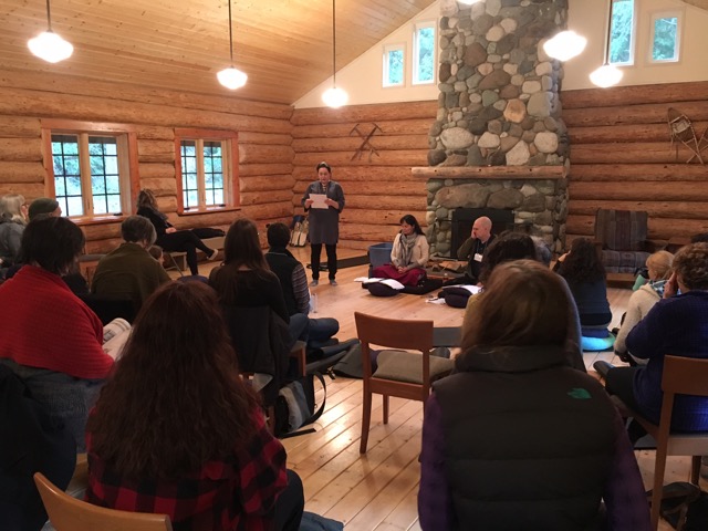 msc-core-skills-port-townsend-wa-mindfulness-compassion-meditation-retreat Several mindfulness teachers sit in front of a large stone fireplace in a tall bright log room, with about a dozen students facing them.