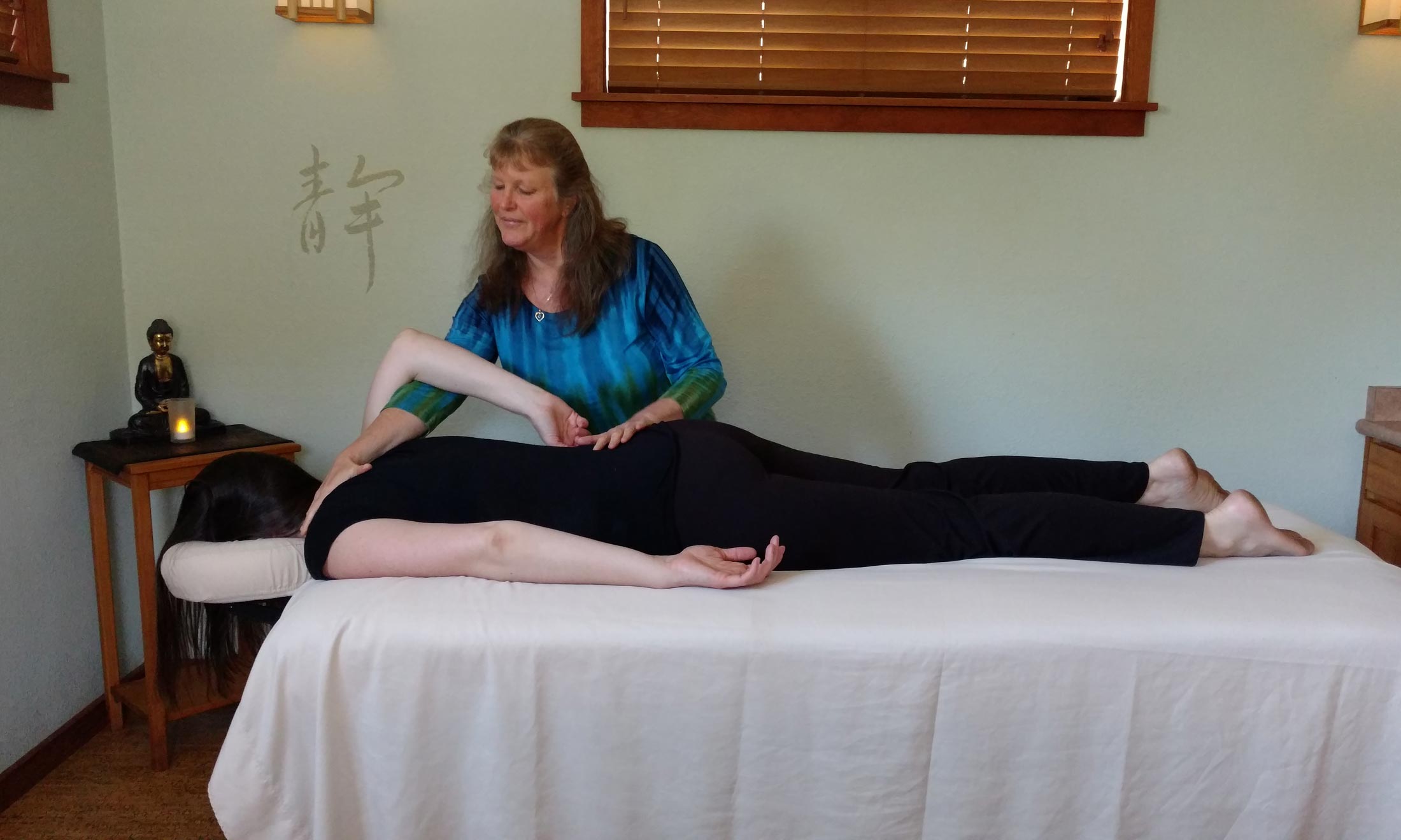 raizelah-bayen-mindful-massage Raizelah Bayen giving a mindful massage to a person laying face down on a massage table wearing black pants and tank top.