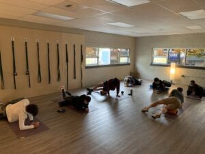 A partial view of the Prime studio space with 7 people stretching on yoga mats and yoga straps on the wall.
